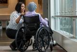 A HSL employee bends over to talk to a patient in a wheelchair. 