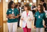 Three female nurses wearing scrubs walk down a hallway together.