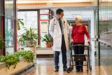 A gray-haired woman with a rollator stands talking to a male doctor in a hallway at Hebrew Rehabilitation Center in Boston.