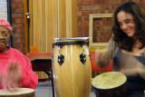 An older woman and a music therapist smile as they play the drums.