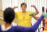 Two senior women lift small weights, following the instruction of their class leader.