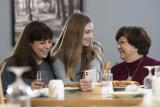 Grandmother, mother, and daughter sitting at a dinner table and looking at the daughter's cell phone. 