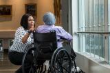 Woman kneels next to person in wheelchair.