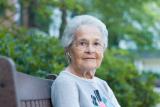 Woman with glasses and serious expression sitting on bench outside.