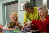 Art instructor showing two smiling women how to make colorful paper mache bowls