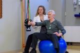 Patient sitting on a ball and doing an arm exercise under the guidance of a medical staff person.