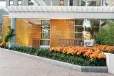 Entryway of Goldman Residences at 1550 Beacon Place, Brookline, MA- Granite textured building with two-tiered white awning, orange tile, benches and orange flowers in raised beds.