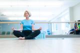 Woman in aqua blue shirt sitting cross-legged, in a meditative pose with the back of her hands on her knees.