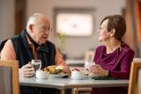 Two seniors sitting at a meal and holding glasses of water