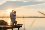 senior couple standing in front of a sunset by the water