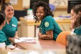 A diverse group of nurses sit around a table smiling.