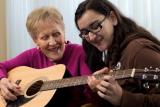 Young girl sitting with senior woman who is playing guitar