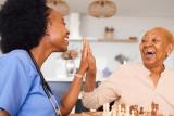 A visiting nurse and an older adult woman share a high five.