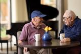 Two older men sitting together at a table in a lounge area.