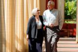 An older man and woman walk down a sunlit corridor.