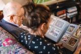 Older man sitting down on a couch looking at a photo album with a woman next to him.