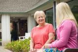 Older woman sitting on a bench outside talking with another woman.