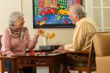 Older man and woman sitting at a table in a lounge area playing checkers.