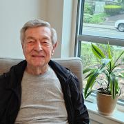 Headshot of CCB resident Bob Boyd while he is sitting by a plant smiling