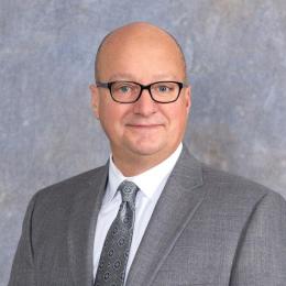 headshot of man in grey suit with silver tie