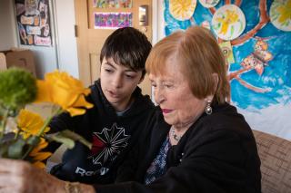 A resident in memory assisted living at NewBridge on the Charles in Dedham, MA arranges flowers with a middle-school aged student.