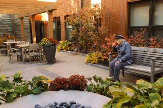 A resident sits outside on a bench and sips his coffee. 