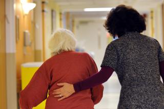 A woman guides a resident using a walker down a hallway.