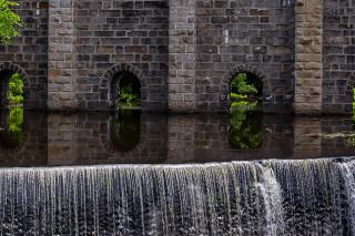 Water flowing through the Canton Viaduct, an arched stone railroad viaduct, and cascading down a spillover.