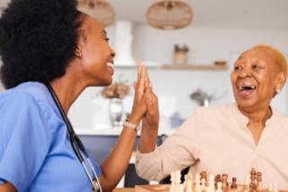 A visiting nurse and an older adult woman share a high five.