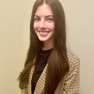 Headshot of woman with long dark hair in tan and black checkered sports coat