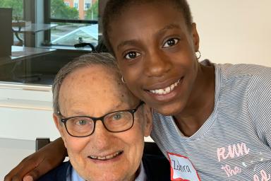 An elder male embraces a child volunteer in a hug as they both smile