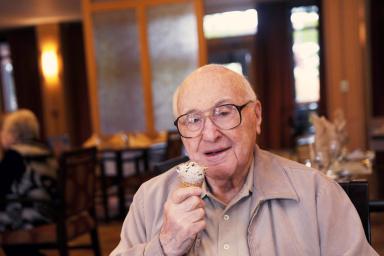 A man with glasses smiles while holding an ice cream cone in a dining room