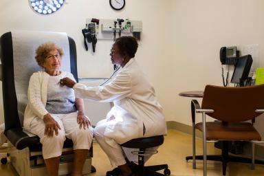 A Hebrew SeniorLife doctor listens to the heartbeat of a community resident in an exam room