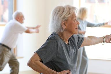 A female resident smiles and holds her hand to her stomach while doing yoga with two other residents
