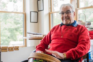 A male resident smiles while playing a drum in a room surrounded by other musical instruments 