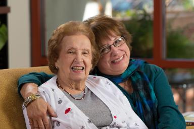 A daughter embraces her mother in a hug while both of them smile