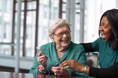 A patient at Hebrew Rehabilitation Center listens to therapeutic music with the help of a life enhancement team member.