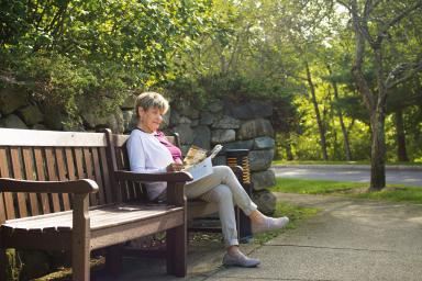A female sits on a bench outside and reads