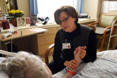 Rabbi Sara Paasche-Orlow sits in a chair and holds a patients hand while talking to her