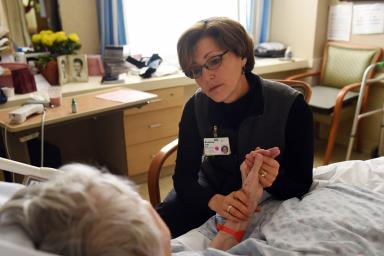 Rabbi Sara Paasche-Orlow  sits in a chair and holds a patients hand while talking to her 