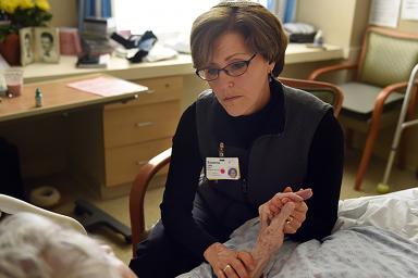 Rabbi Sara Paasche-Orlow  sits in a chair and holds a patients hand while talking to her 