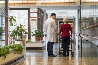 A male doctor talks with older woman using walker in Hebrew Rehabilitation Center hallway