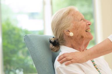 A female resident looks up and smiles as someone pats her shoulder