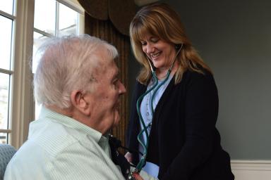 A Home Health worker smiles while checking a male patient's blood pressure