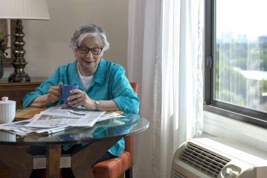 Older woman sitting at a table reading newspaper