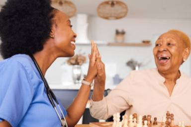 A visiting nurse and an older adult woman share a high five.