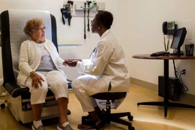 Older woman sitting in doctor office chair seeing a woman doctor