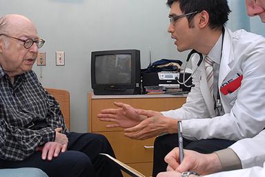 Older man sitting and talking with two doctors.