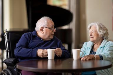 Older man sitting in a wheelchair at a table having coffee with an older woman
