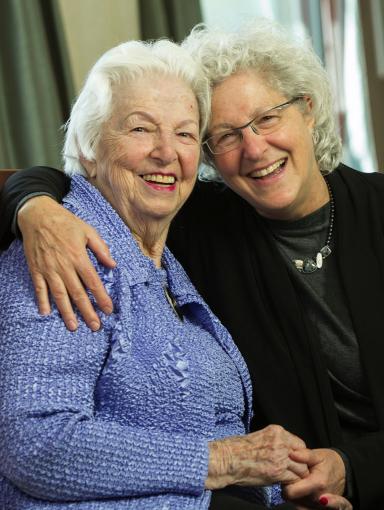 Two women embracing and holding hands, smiling at the camera.